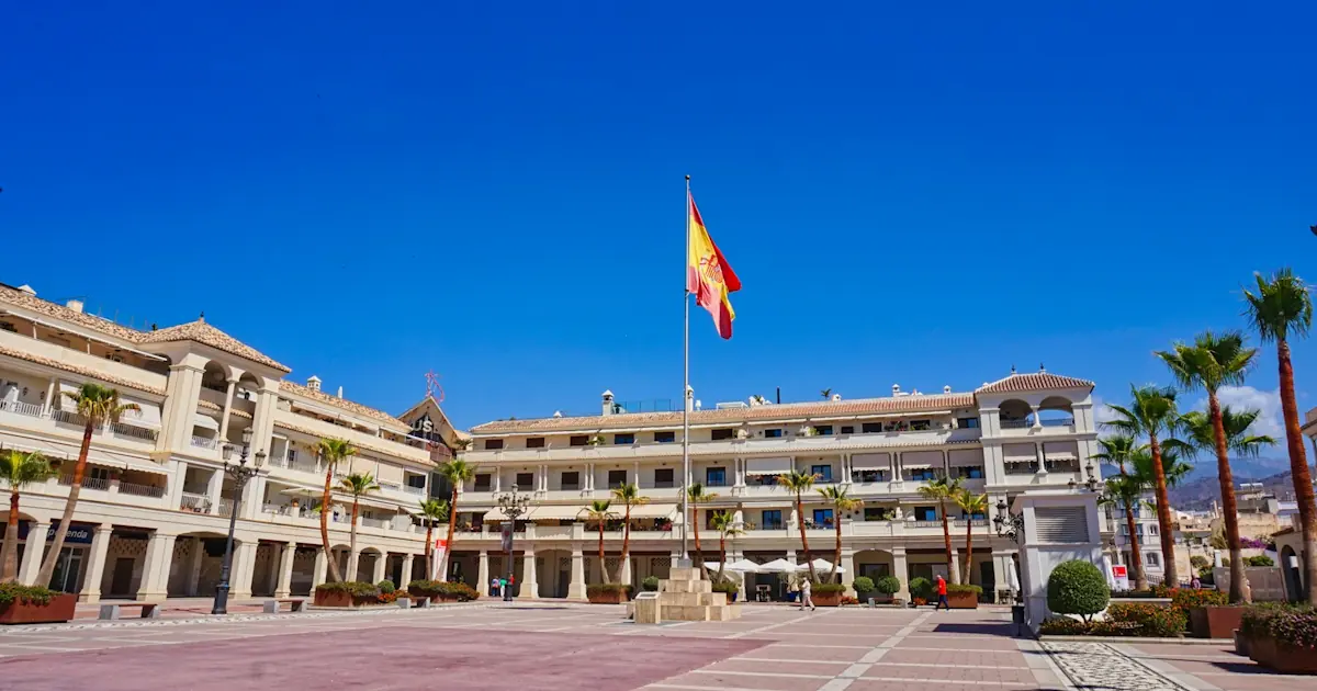 A huge square with a big building, a spanish flag and some palm trees in Nerja on a sunny day