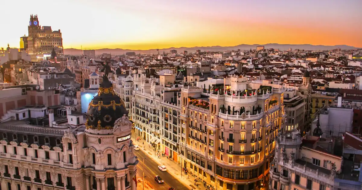 Sunlit apartment balconies on a dense Spanish city street, suggesting urban rent and everyday cost-of-living choices.