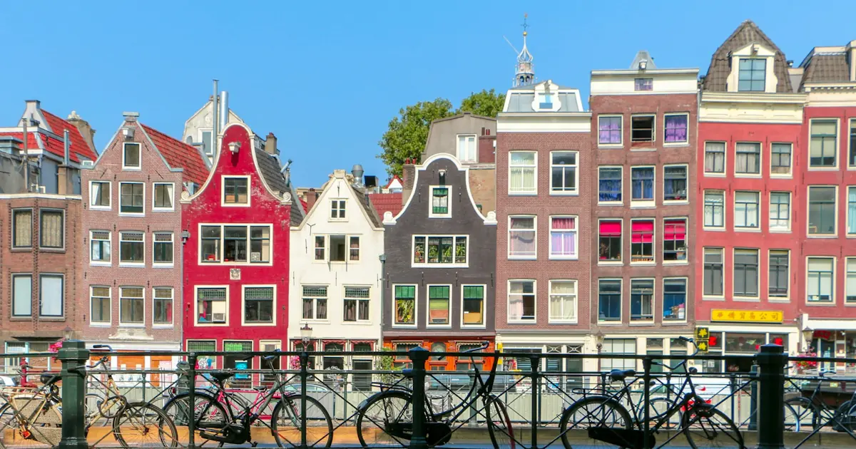 A row of narrow canal houses in Amsterdam reflected in still water on a clear morning.