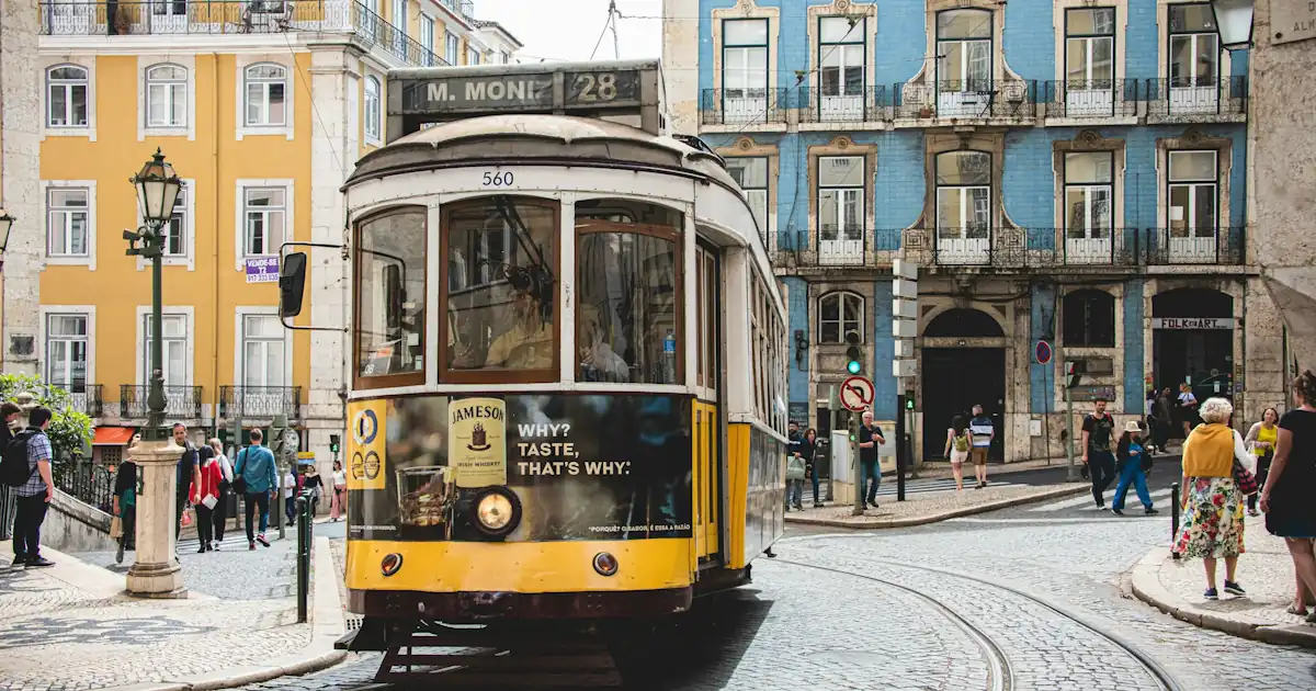 Yellow tram on a cobblestone street in Lisbon with pastel buildings