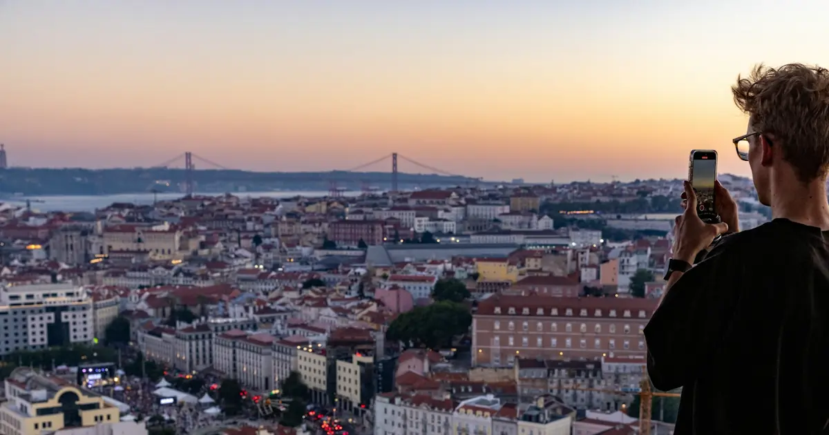 Person using a smartphone while taking a cell phone photo of a bridge in Lisbon